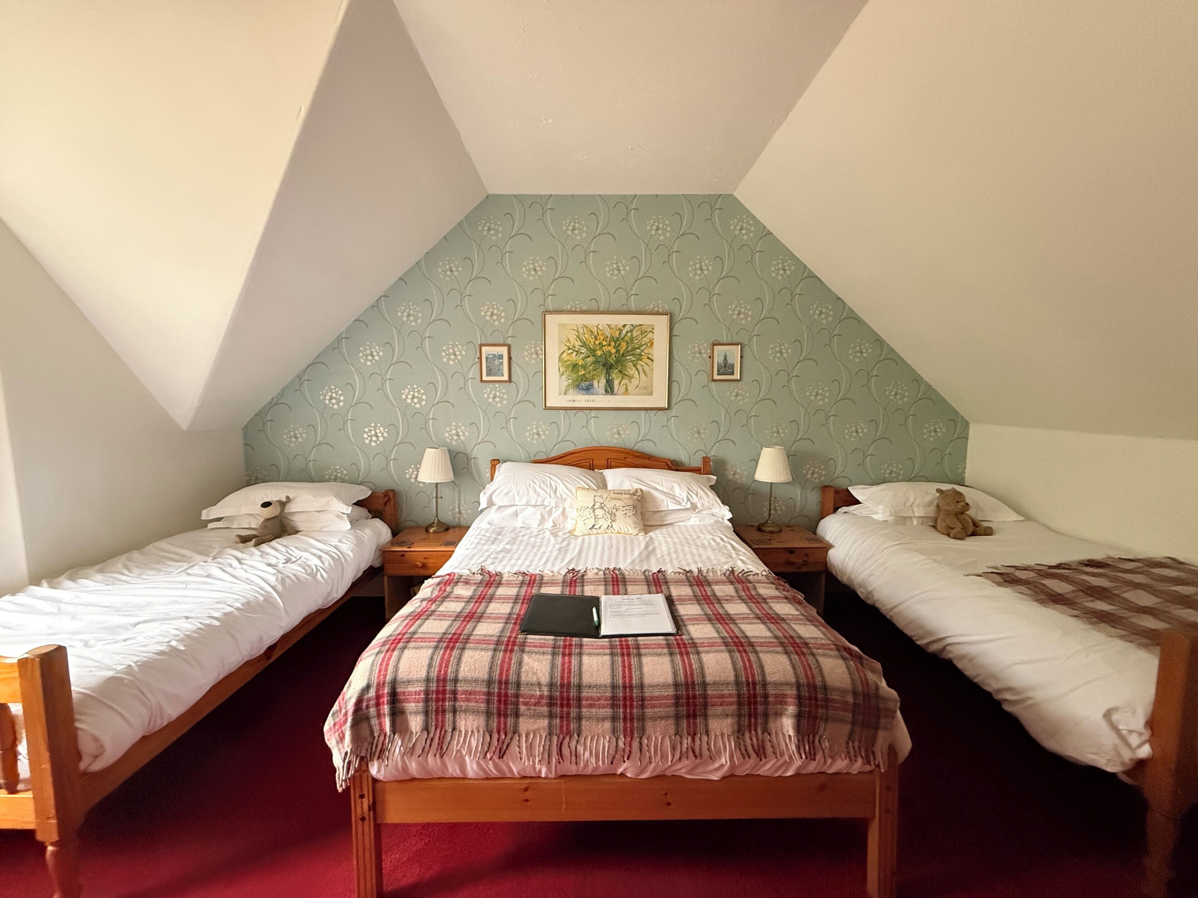 A room with two single beds, a larger bed with a plaid blanket, and a wooden headboard.