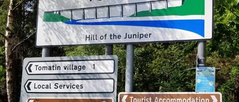 A signpost with directions to Tomatin village, local services, Tomatin Distillery Visitor Centre, and tourist accommodations including Glenan Lodge Guest House.