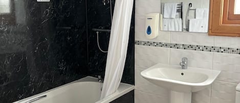 Een moderne badkamer met een douchewand van zwart marmer, een witte badkuip, een wit wastafelmeubel en een spiegel boven het wastafelmeubel.