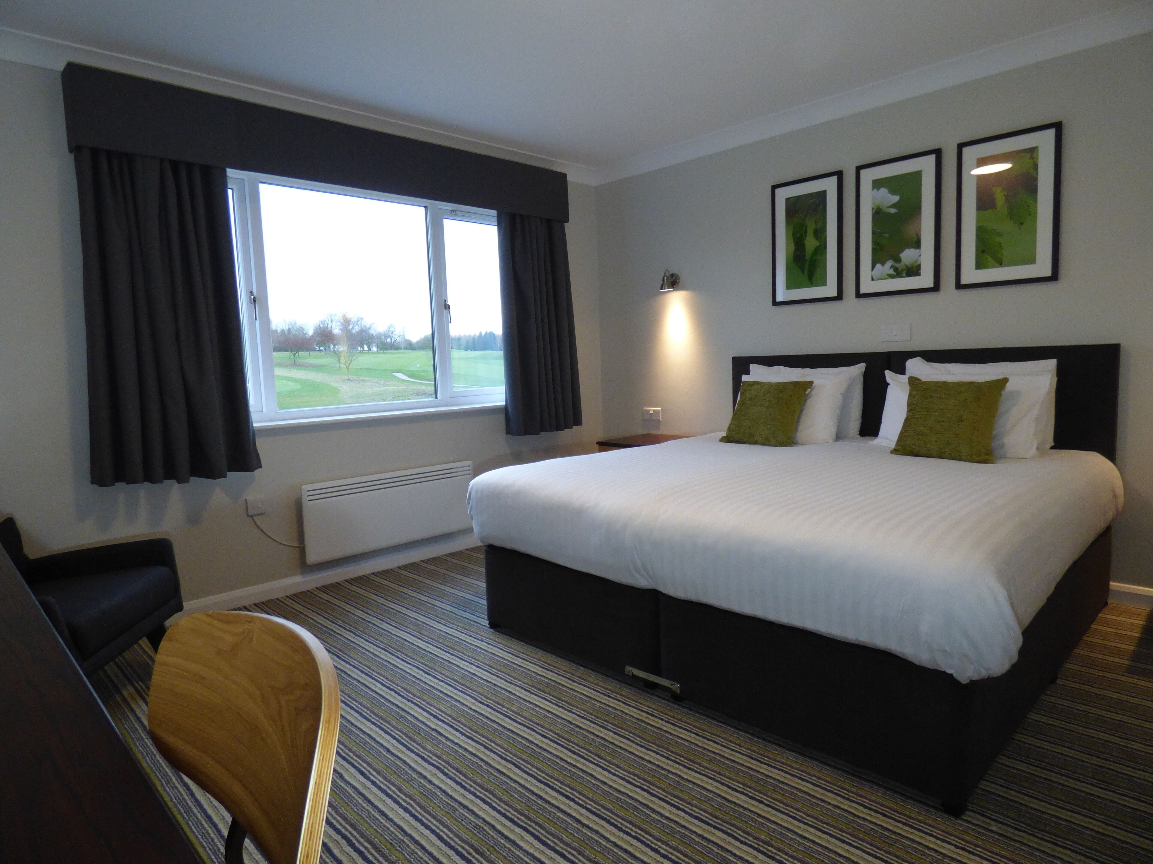 A hotel room with a large bed, a desk, and a window with curtains.