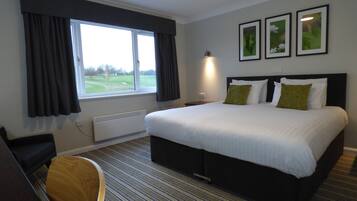 A hotel room with a large bed, a desk, and a window with curtains.