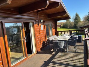 A wooden deck with a table and chairs, a glass door leading to a room, and a number '3' sign. - Greetham Valley Hotel (Oakham)