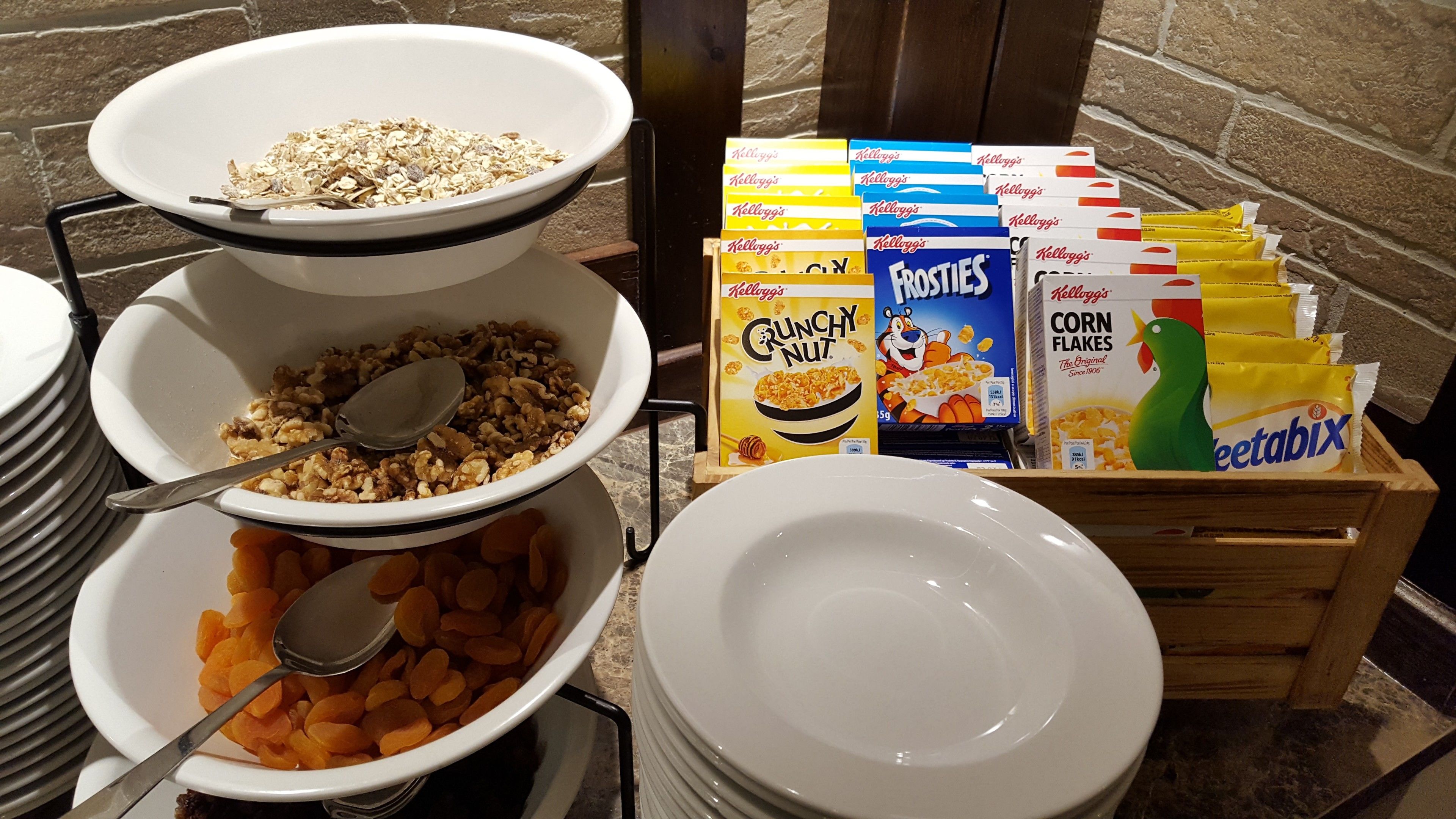A breakfast buffet with bowls of cereal, nuts, and dried fruits, and boxes of Kellogg's products.