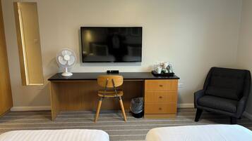 Ein Hotelzimmer mit Bett, Schreibtisch mit Stuhl, Fernseher, Ventilator und Sessel.