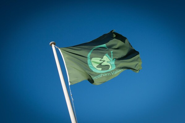 Una bandera con un logotipo y texto en un asta, sobre un cielo azul despejado.