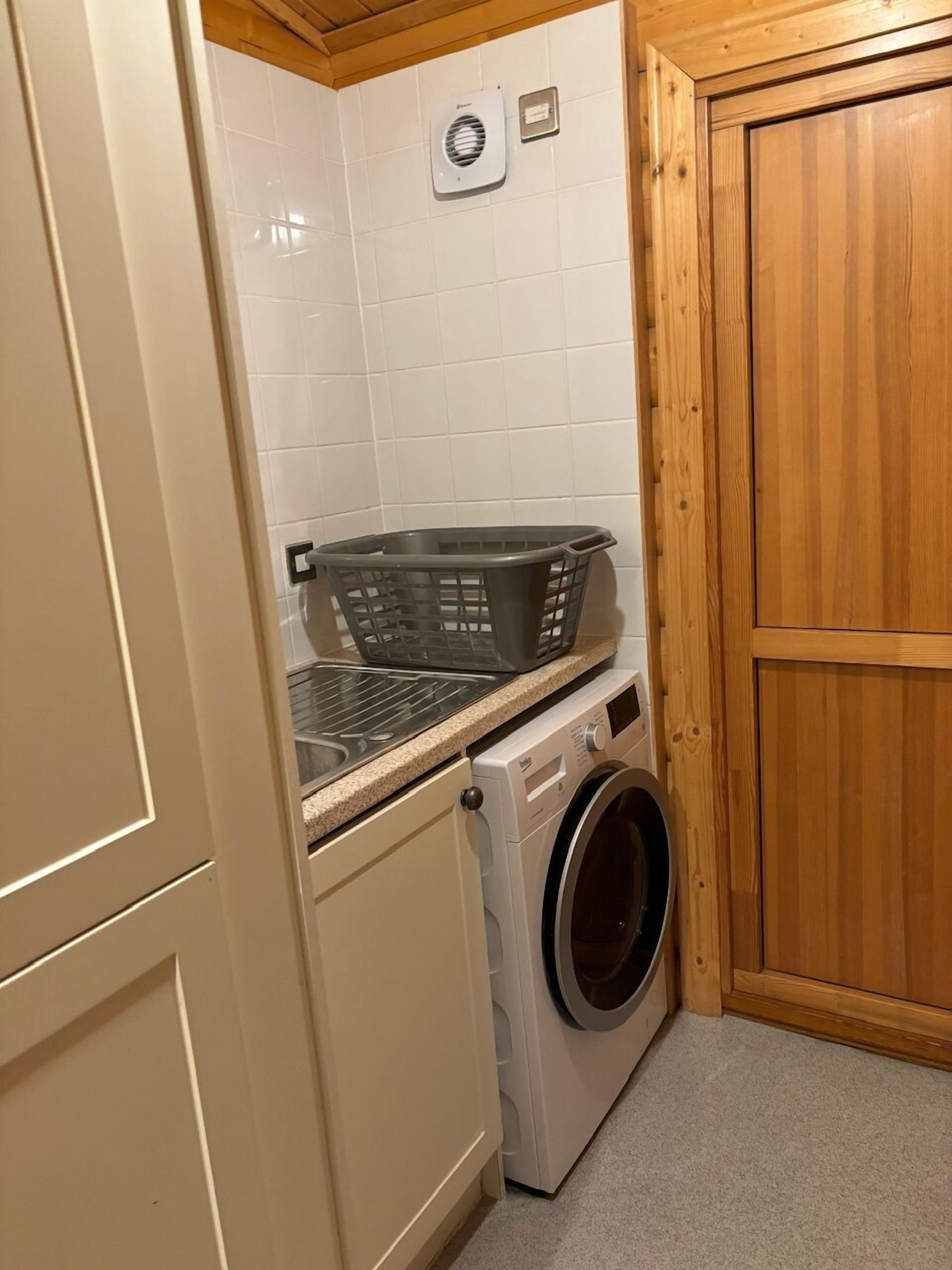 A compact laundry area with a washing machine, a drying rack, and a small heater on the wall.