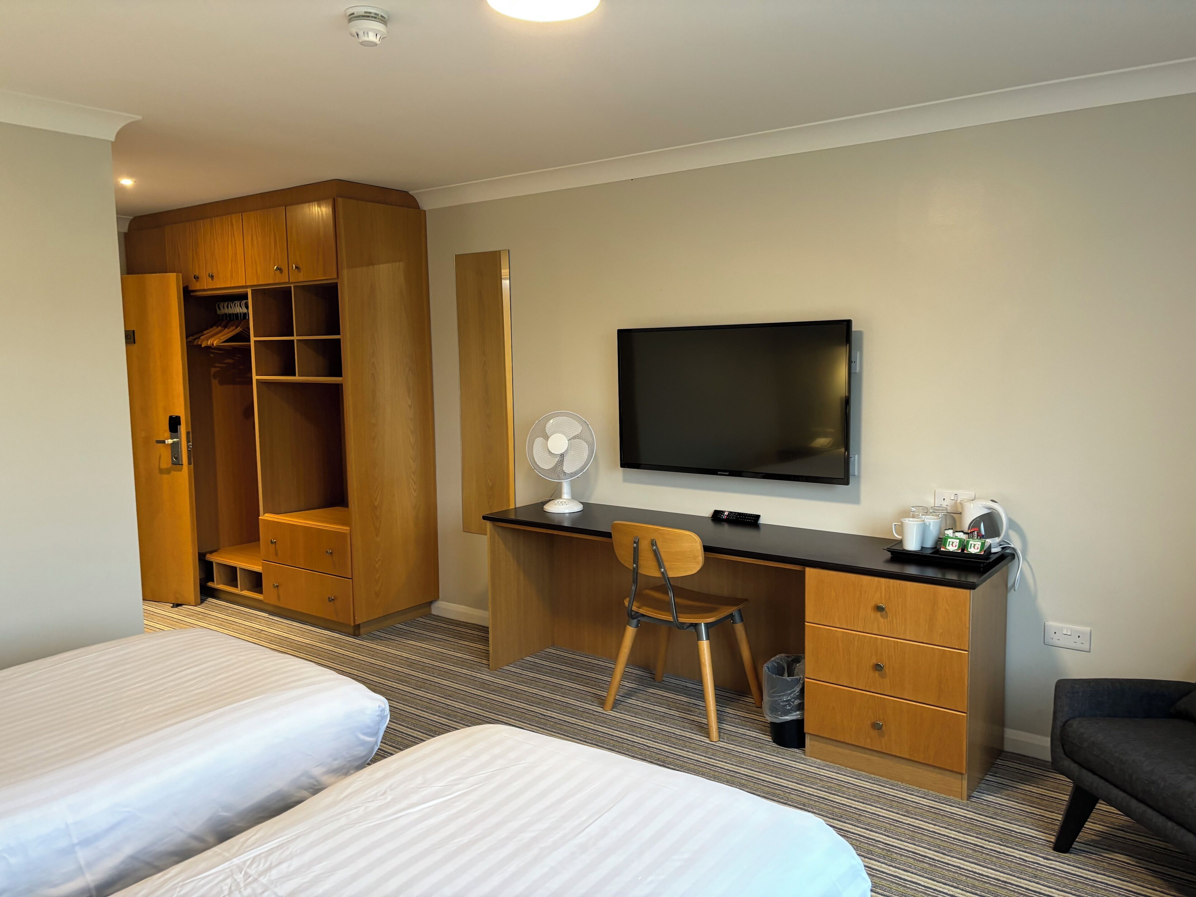 Ein Hotelzimmer mit Bett, Schreibtisch mit Stuhl, Fernseher und Kleiderschrank.