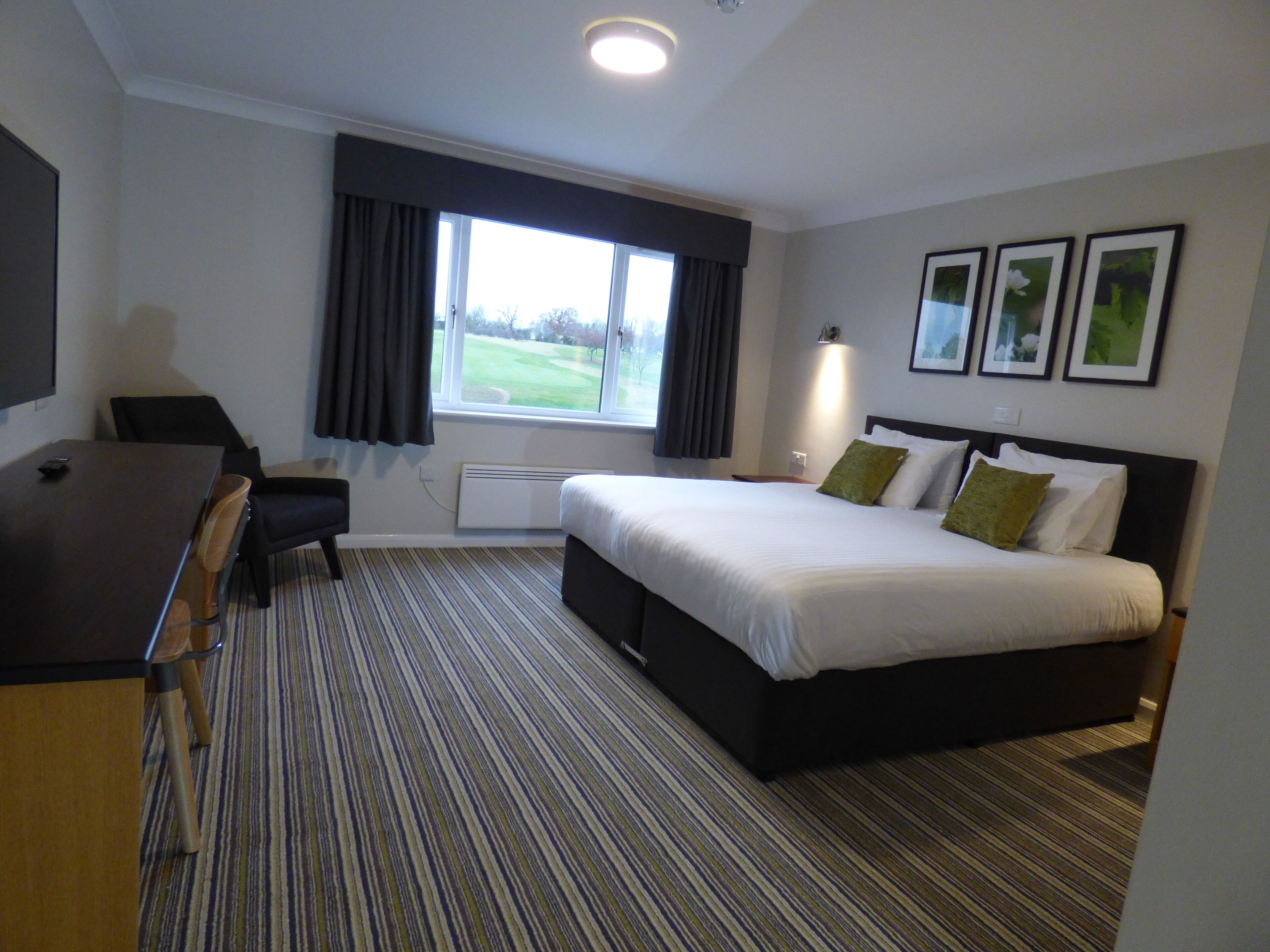 Een hotelkamer met een groot bed, een bureau en een raam met gordijnen.