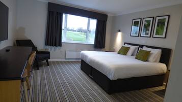 Een hotelkamer met een groot bed, een bureau en een raam met gordijnen.