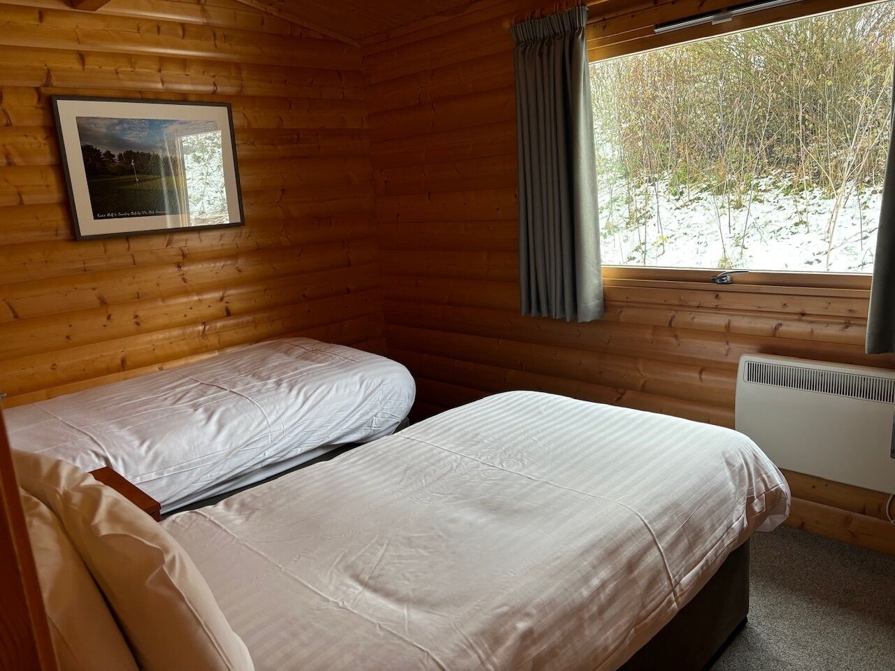 Una habitación tipo cabaña con dos camas, un cuadro en la pared, una ventana con cortinas y un radiador.