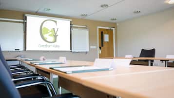 A conference room with a projector screen displaying 'Greetham Valley' logo, a whiteboard, a wooden table, and black chairs.