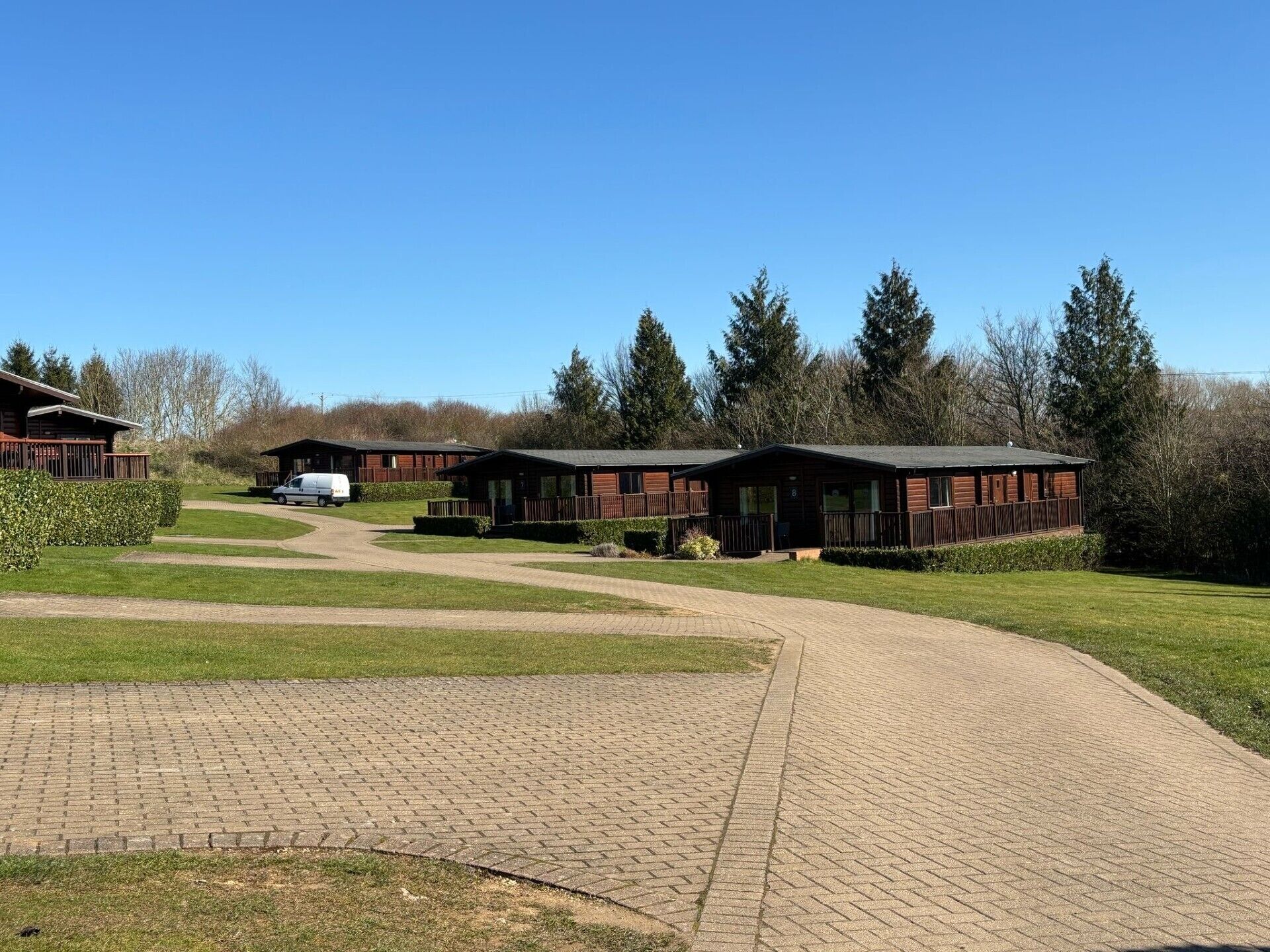 Een rij houten huisjes met een verharde looppad ernaartoe, omgeven door groen en bomen.