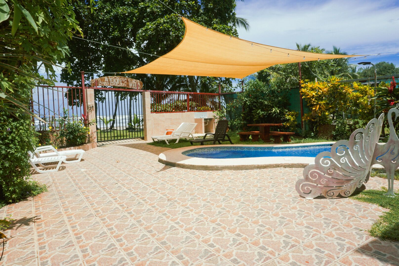 A pool area with tiled flooring, a pergola, and a decorative metal sculpture.
