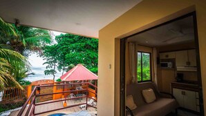 A balcony with a view of the ocean, a red umbrella, and a dining area with chairs. - Hotel La Dolce Vita (Parrita)