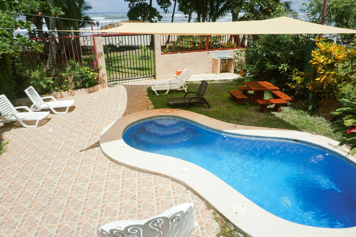 Ein Pool mit Fliesen umgeben, Liegestühle und eine überdachte Terrasse.