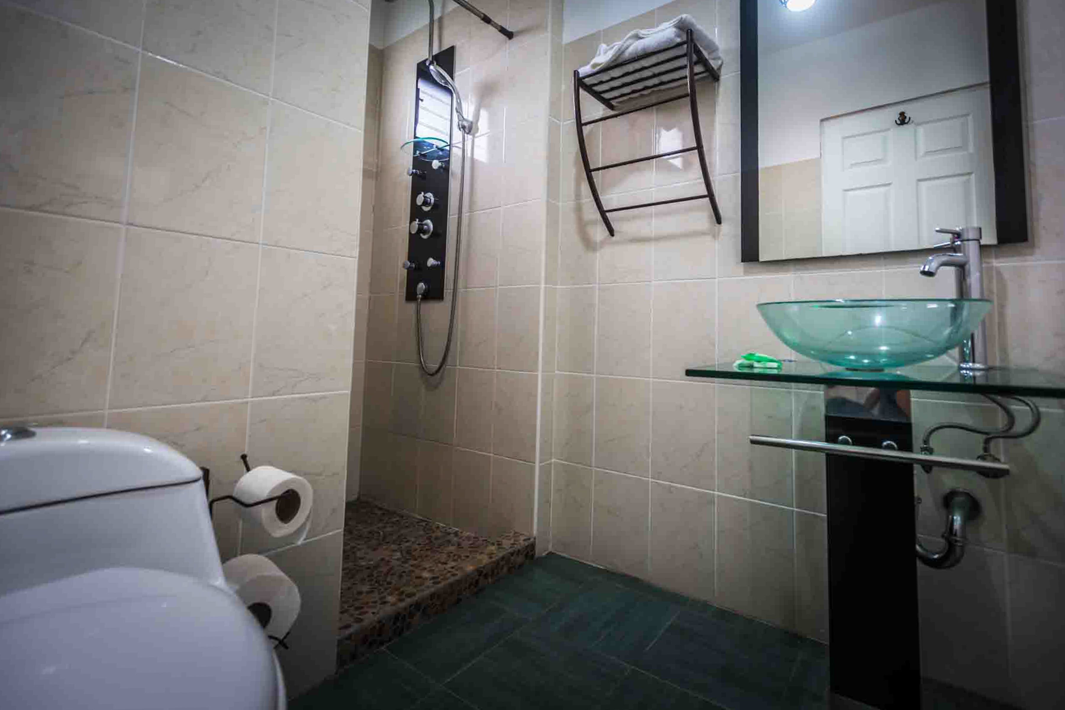 Un baño con lavamanos de vidrio, un perchero, un inodoro y una ducha con panel de control.