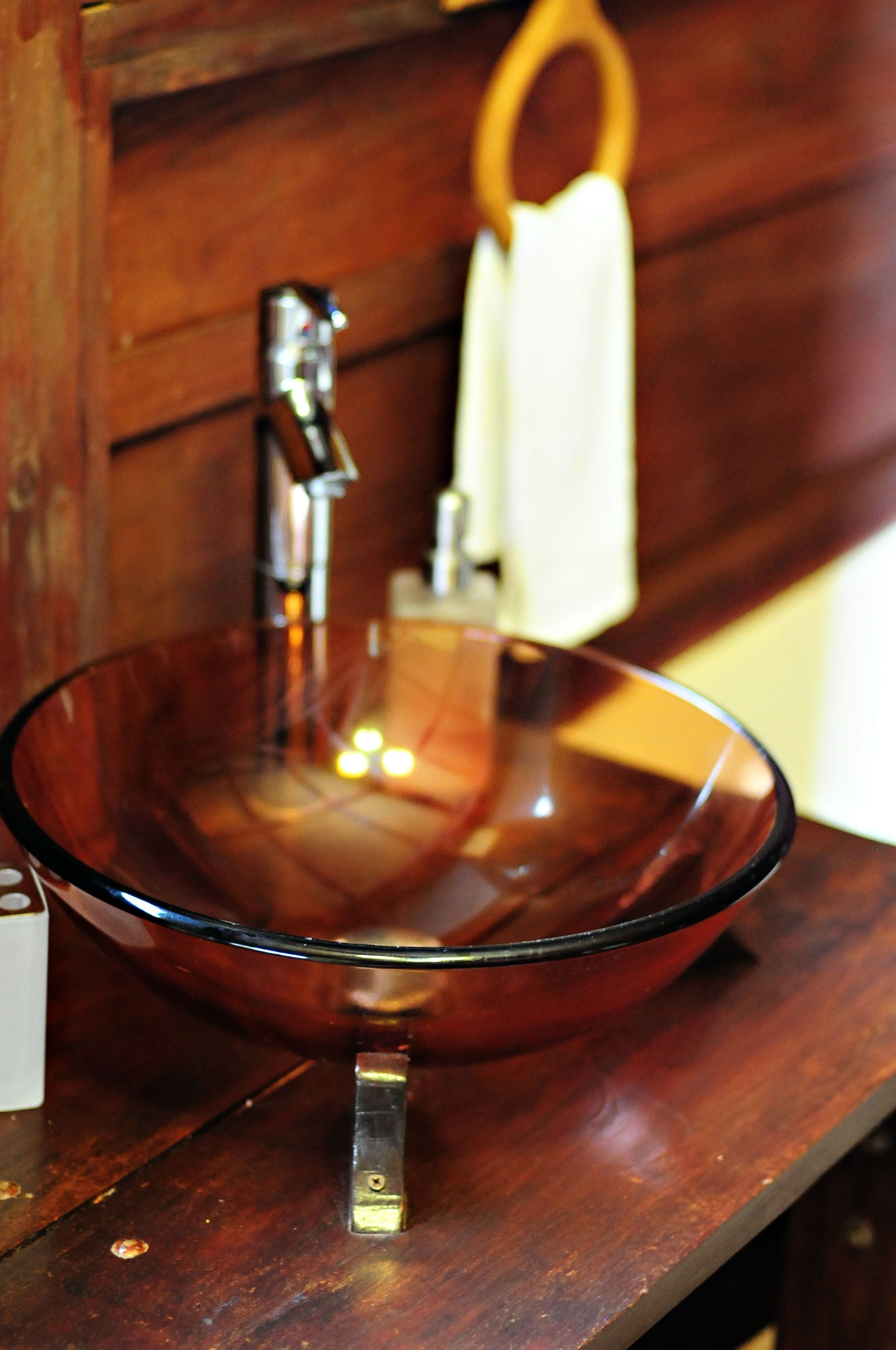 A clear glass bowl sink mounted on a wooden countertop with a metal faucet.