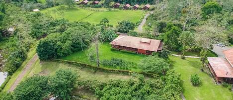 Luchtbeeld van een resort met verschillende cabins met rode daken, een groot centraal gebouw en weelderige groene omgeving.