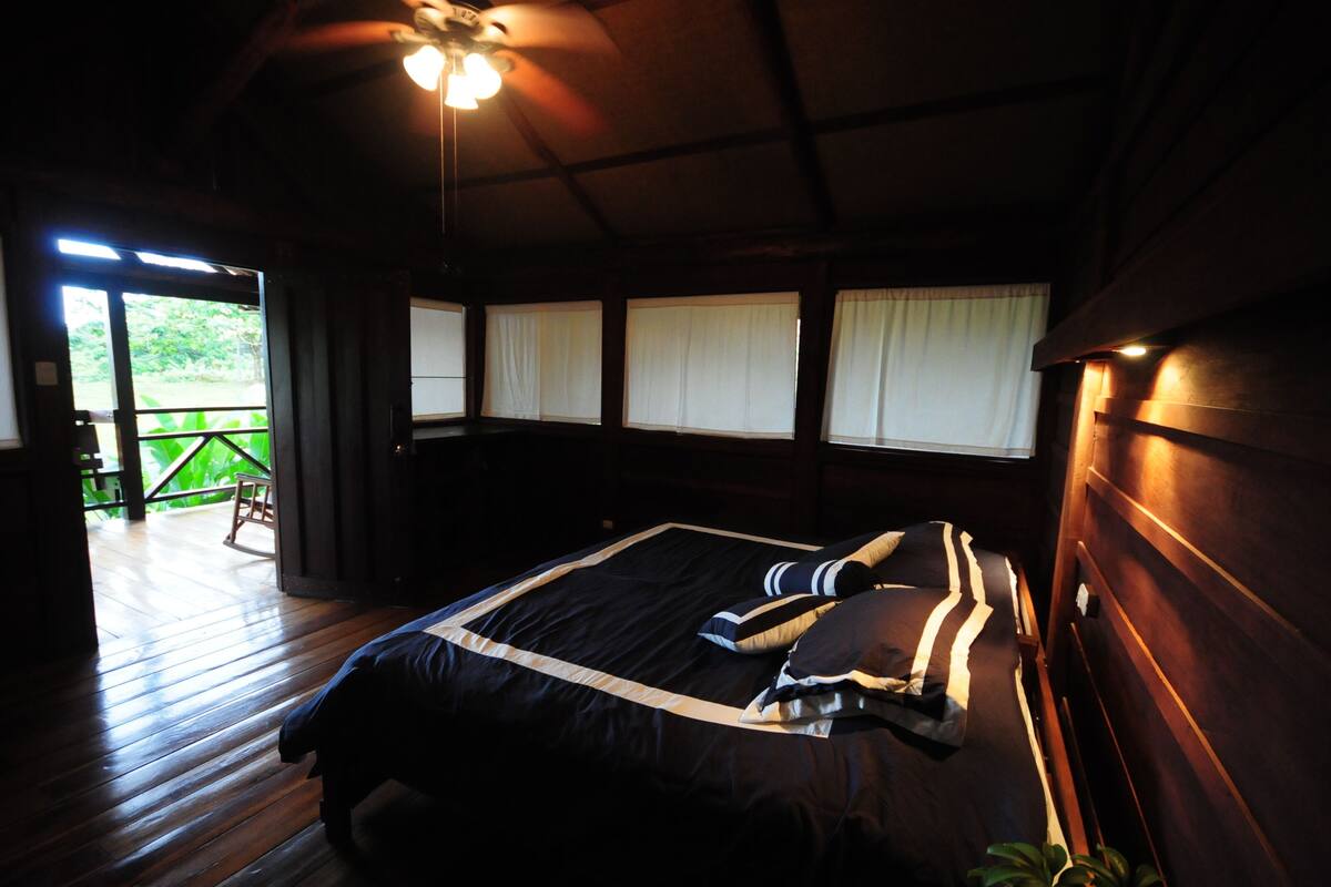 A bedroom with a wooden bed, a ceiling fan, and a view of a wooden deck through a sliding door.