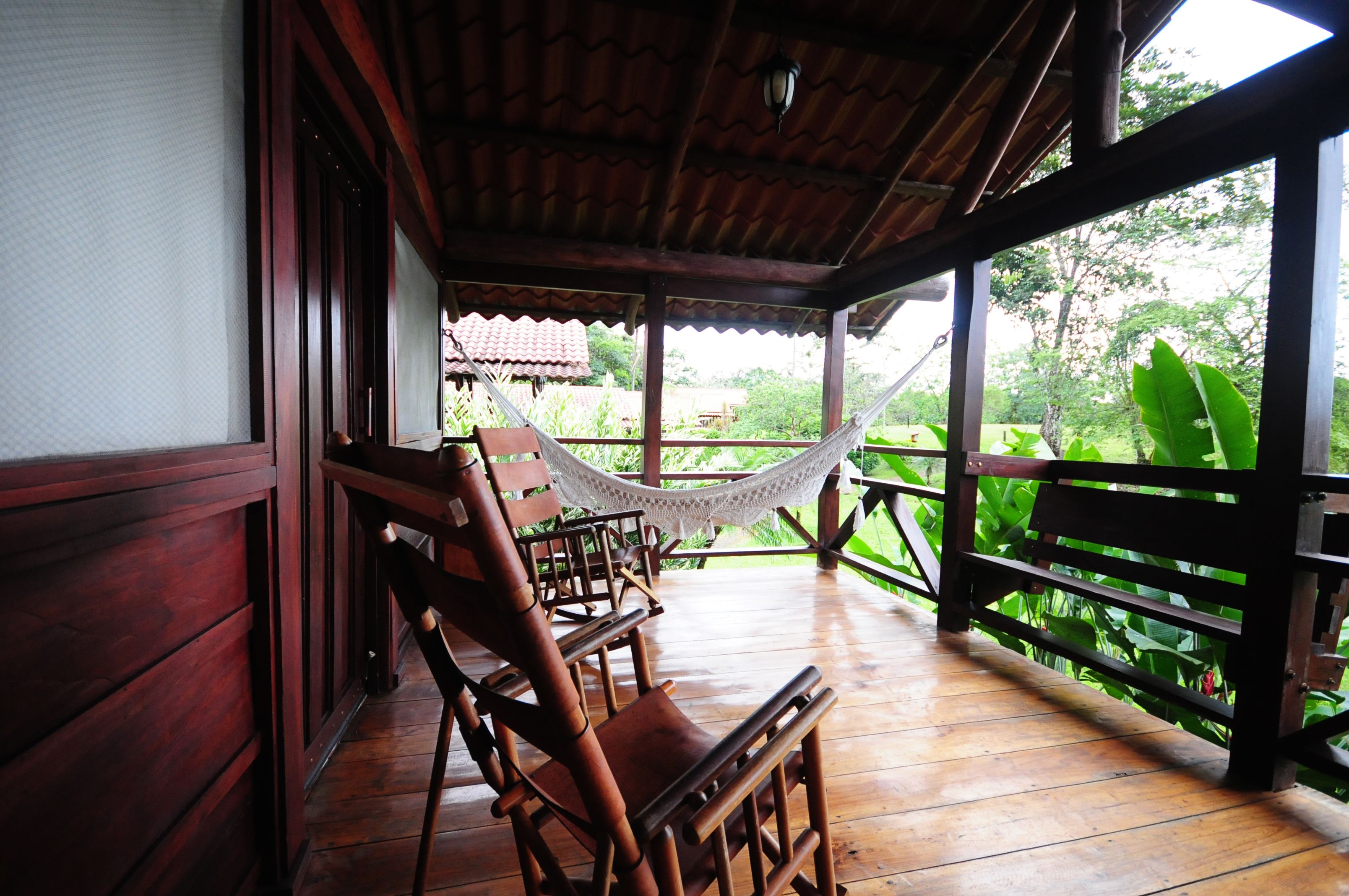 A wooden deck with chairs and a hammock, overlooking a lush garden.