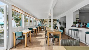 Un comedor amplio con mesas y sillas de madera, ventanas grandes y una zona de bar con taburetes.