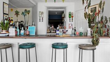 Een bar met krukken, een toonbank vol flessen en decoratieve planten.