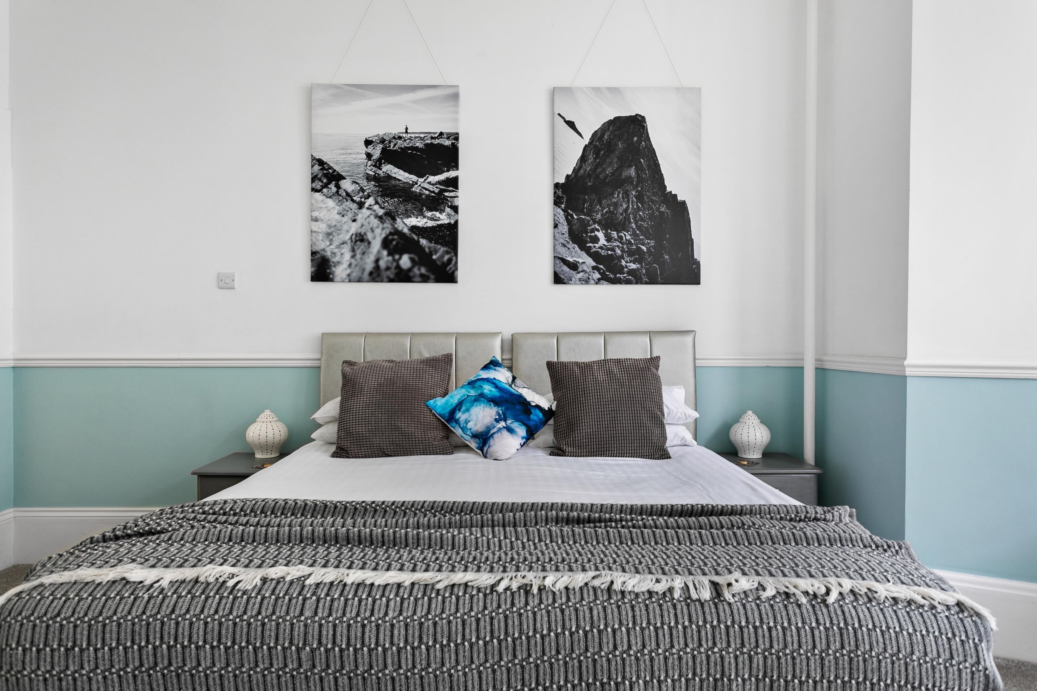 A bedroom with a bed, two wall-mounted pictures, and a nightstand with a lamp.