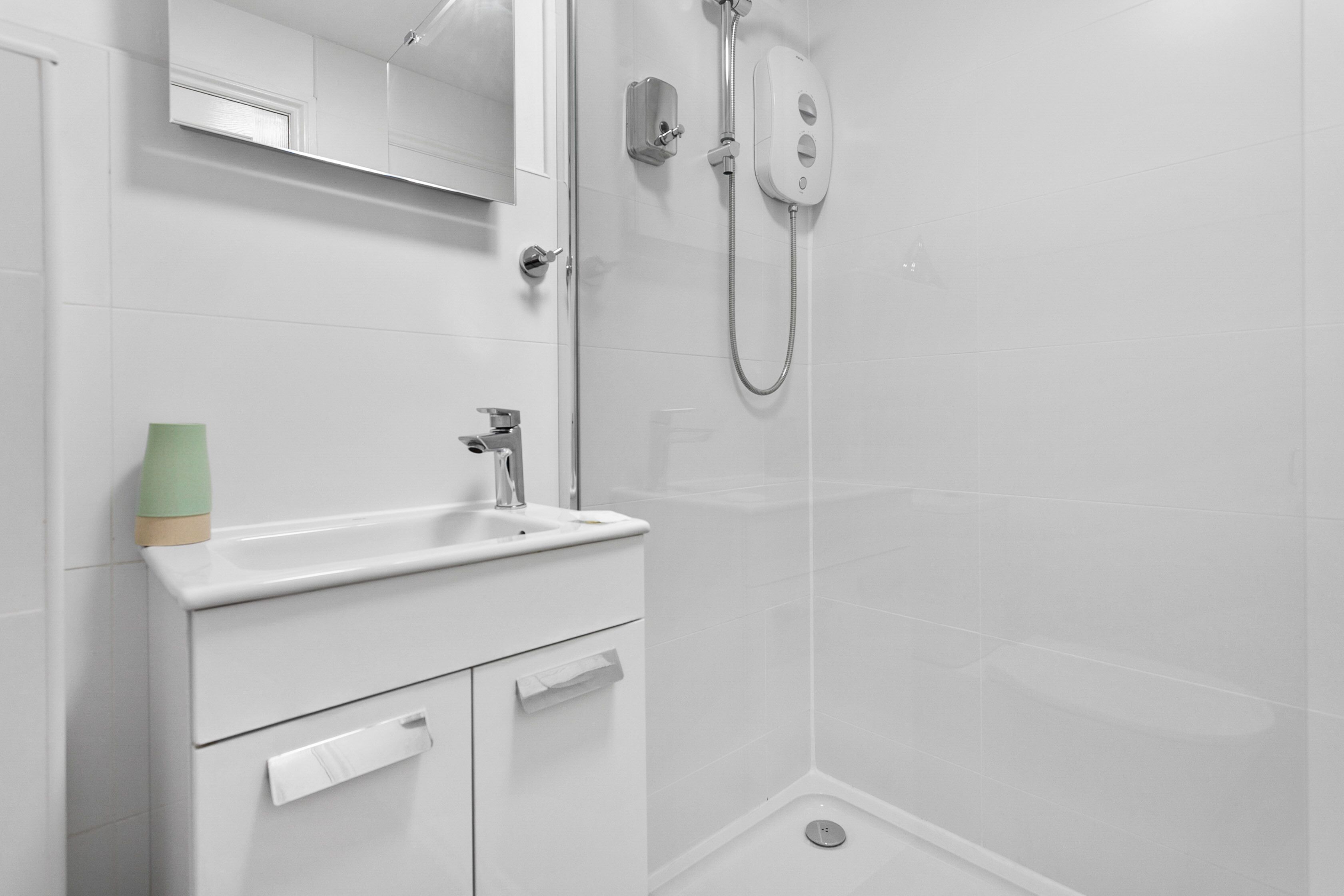 Une salle de bain moderne avec un lavabo blanc, un miroir et une douche.