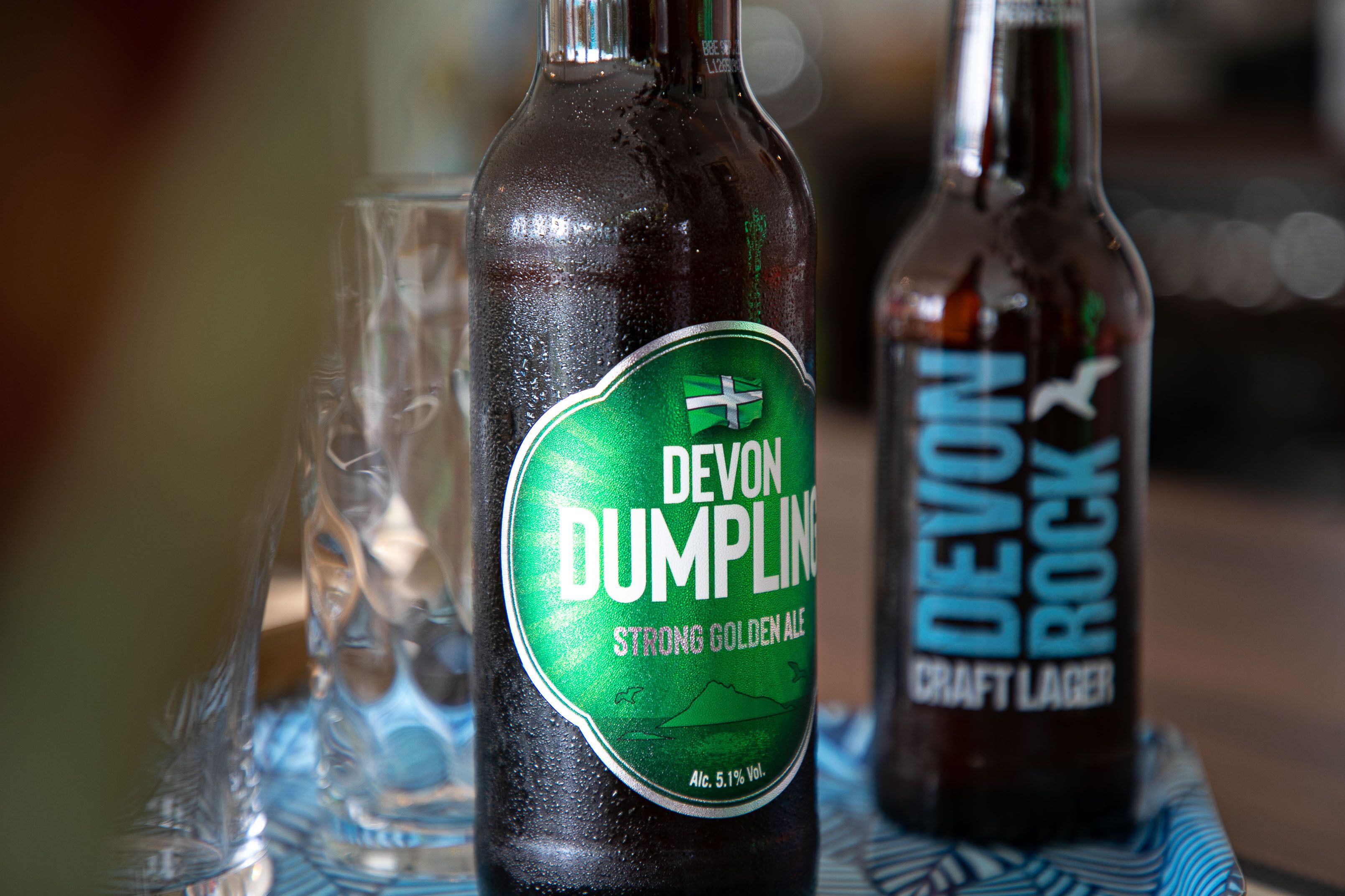 Two bottles of Devon Dumplin Strong Golden Ale and Devon Rock Craft Lager on a table with glasses.