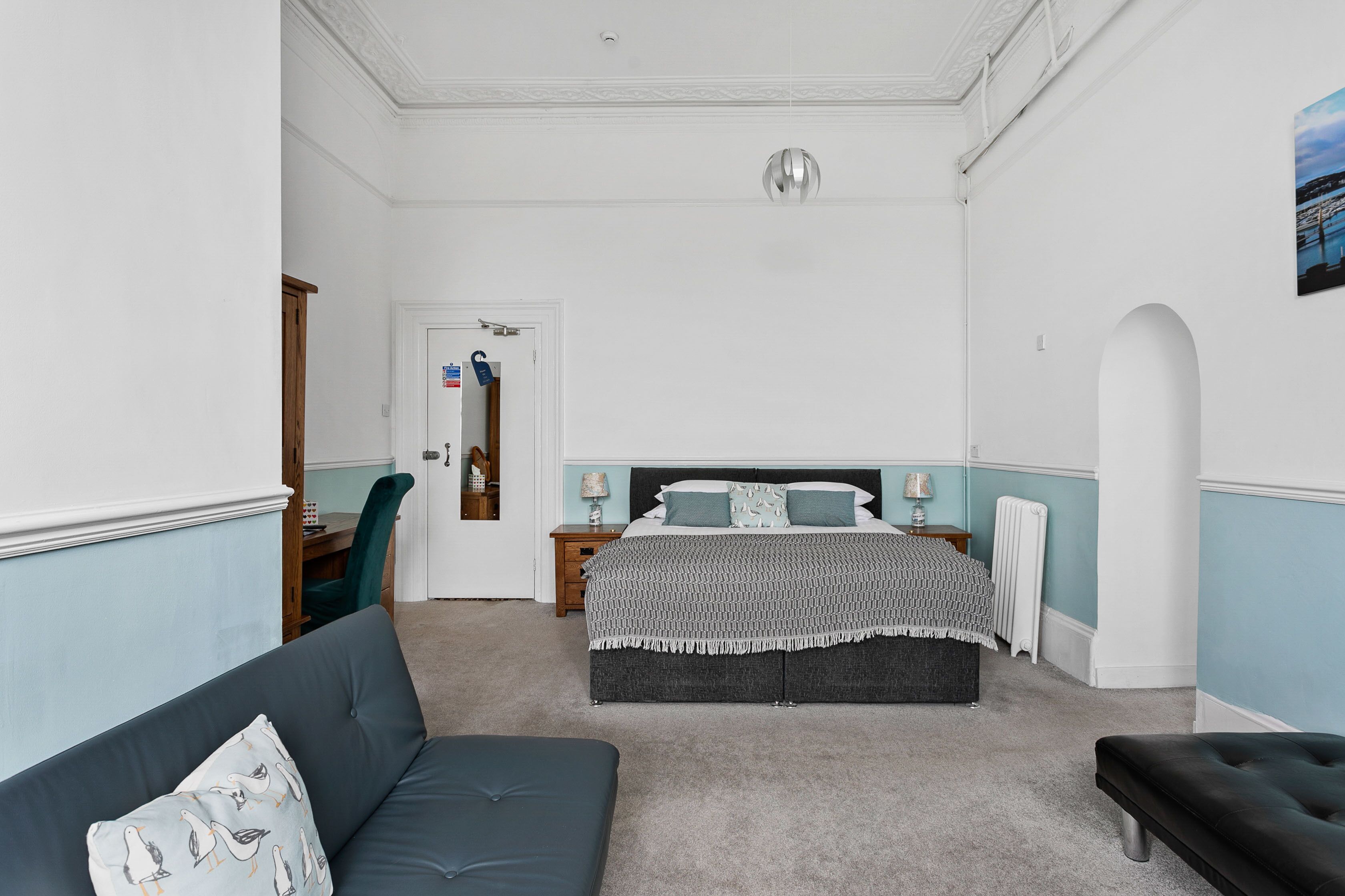 A bedroom with a bed, a sofa, and a bench. There is a door leading to another room.