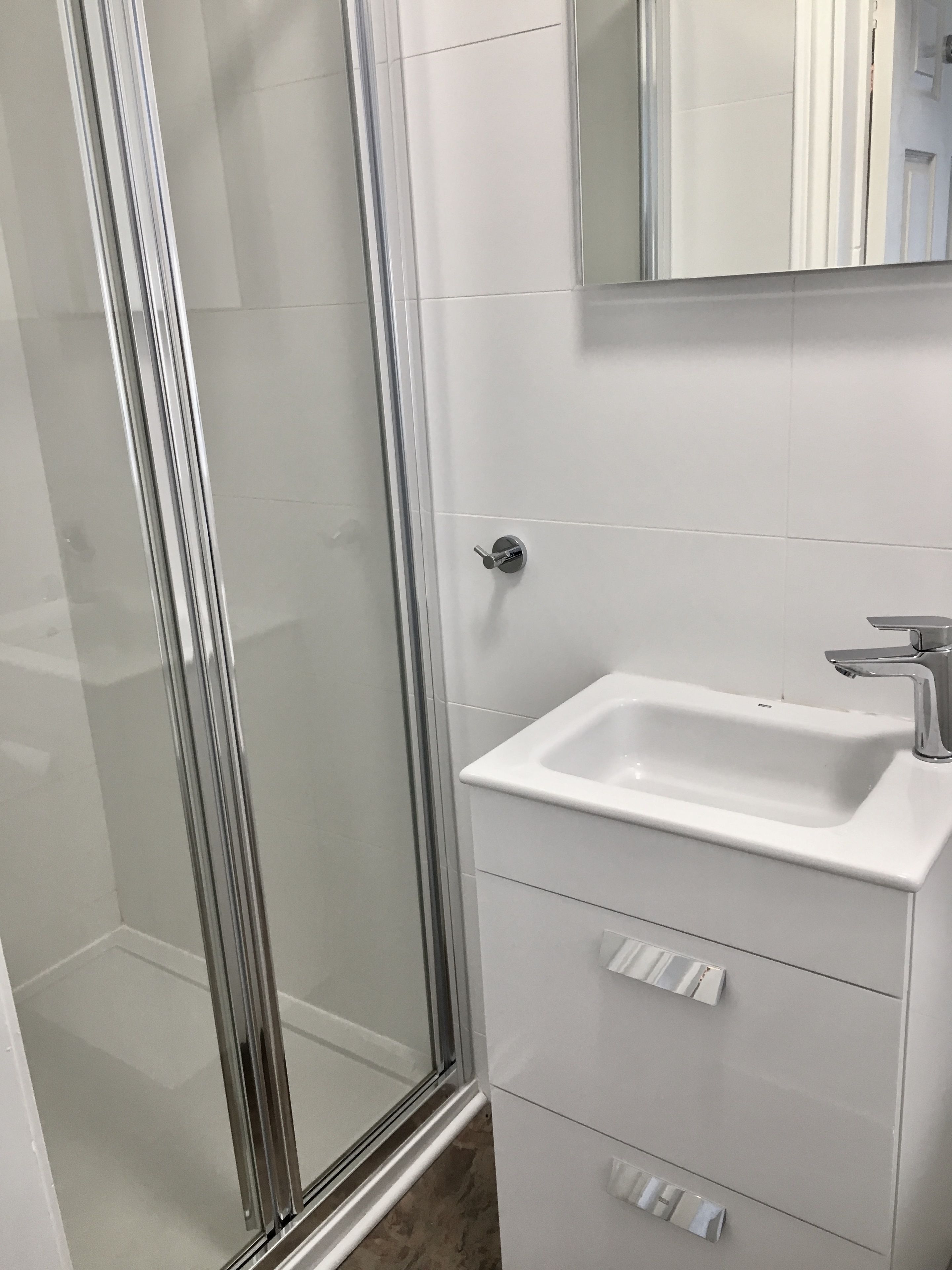 A bathroom with a glass shower enclosure, a white sink, and a mirror above the sink.