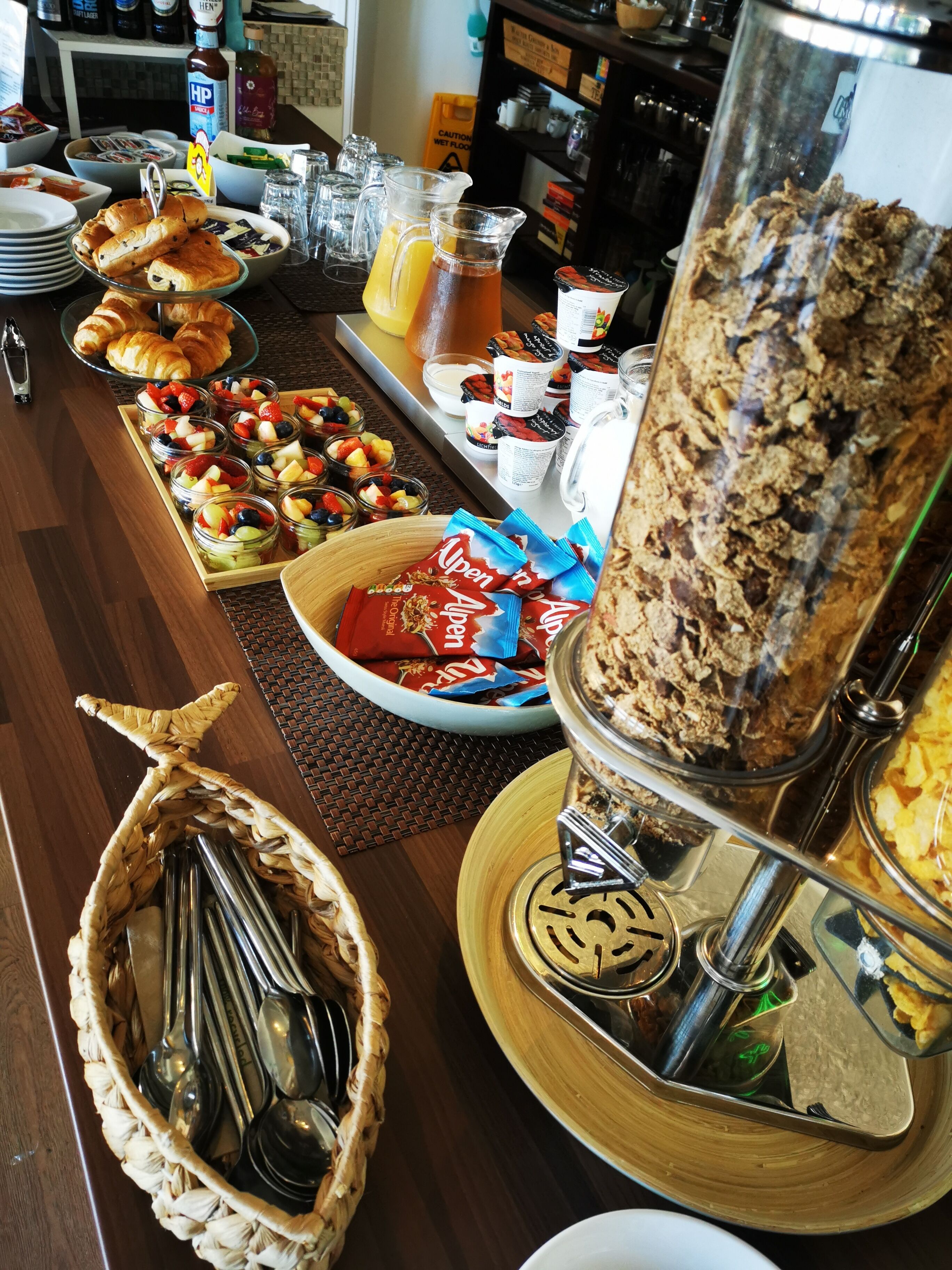 A buffet with various food items including fruits, pastries, and a large container of cereal.