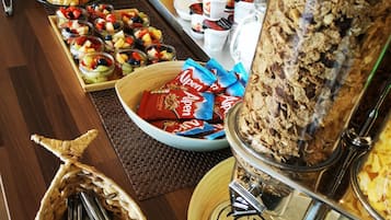 A buffet with various food items including fruits, pastries, and a large container of cereal.