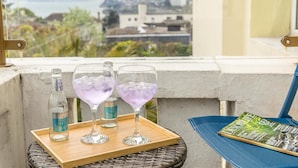 Un balcón con vistas a la ciudad, dos vasos de agua tónica y una revista sobre una silla.