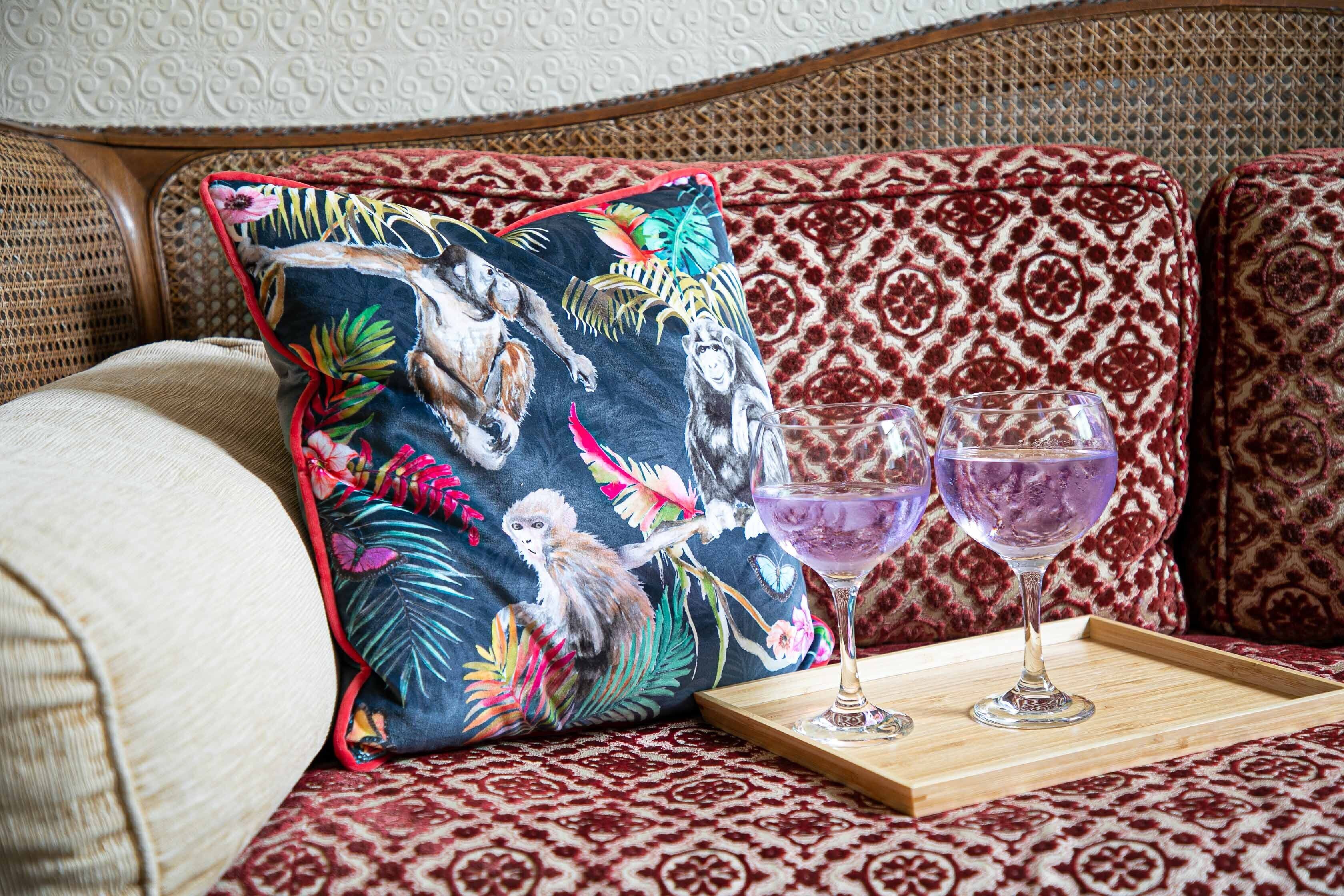 A sofa with patterned cushions, a tray with two glasses, and a decorative pillow with a tropical print.