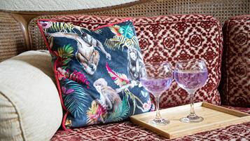 A sofa with patterned cushions, a tray with two glasses, and a decorative pillow with a tropical print.