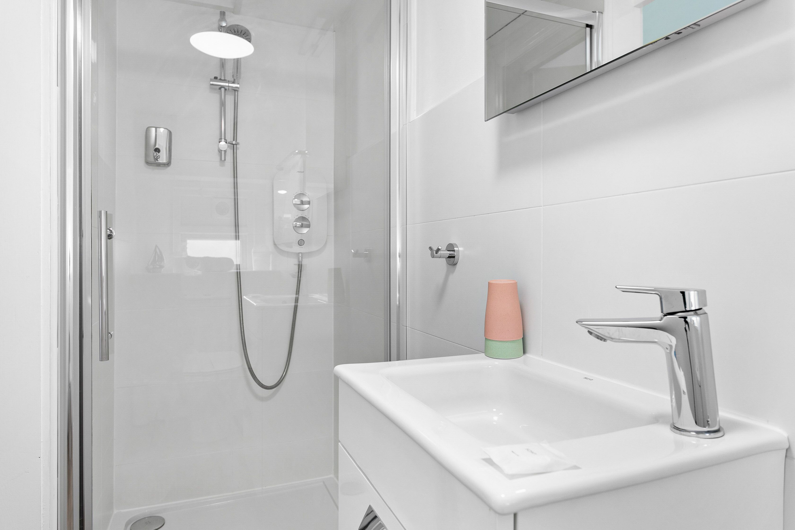 Een moderne badkamer met een douche met glazen wand, een wit wastafelmeubel met een chromen kraan en een spiegel erboven.