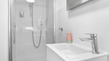 Een moderne badkamer met een douche met glazen wand, een wit wastafelmeubel met een chromen kraan en een spiegel erboven.