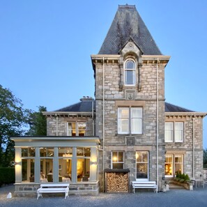 A stone building with a large windowed front, a chimney, and a small outdoor seating area. - Knockendarroch Hotel (Pitlochry)