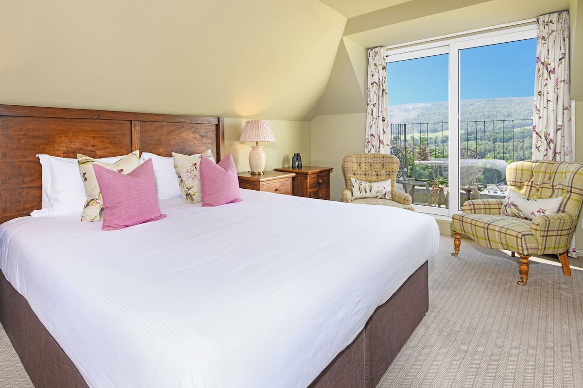 A hotel room with a large bed, two bedside tables, a chair, and a window with a view of the countryside.