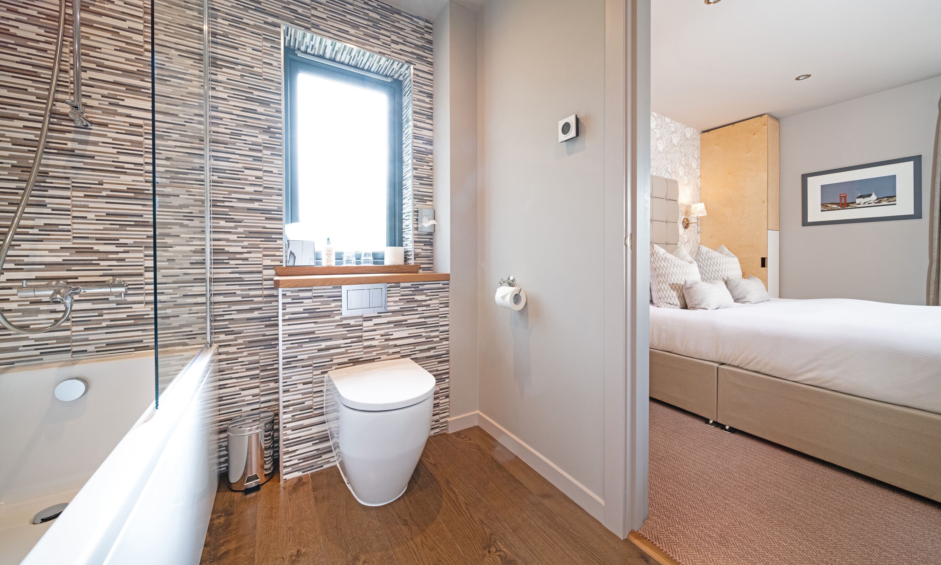Et moderne badeværelse med bruser, toilet og vask. Der er et træskab og et vindue over vasken.
