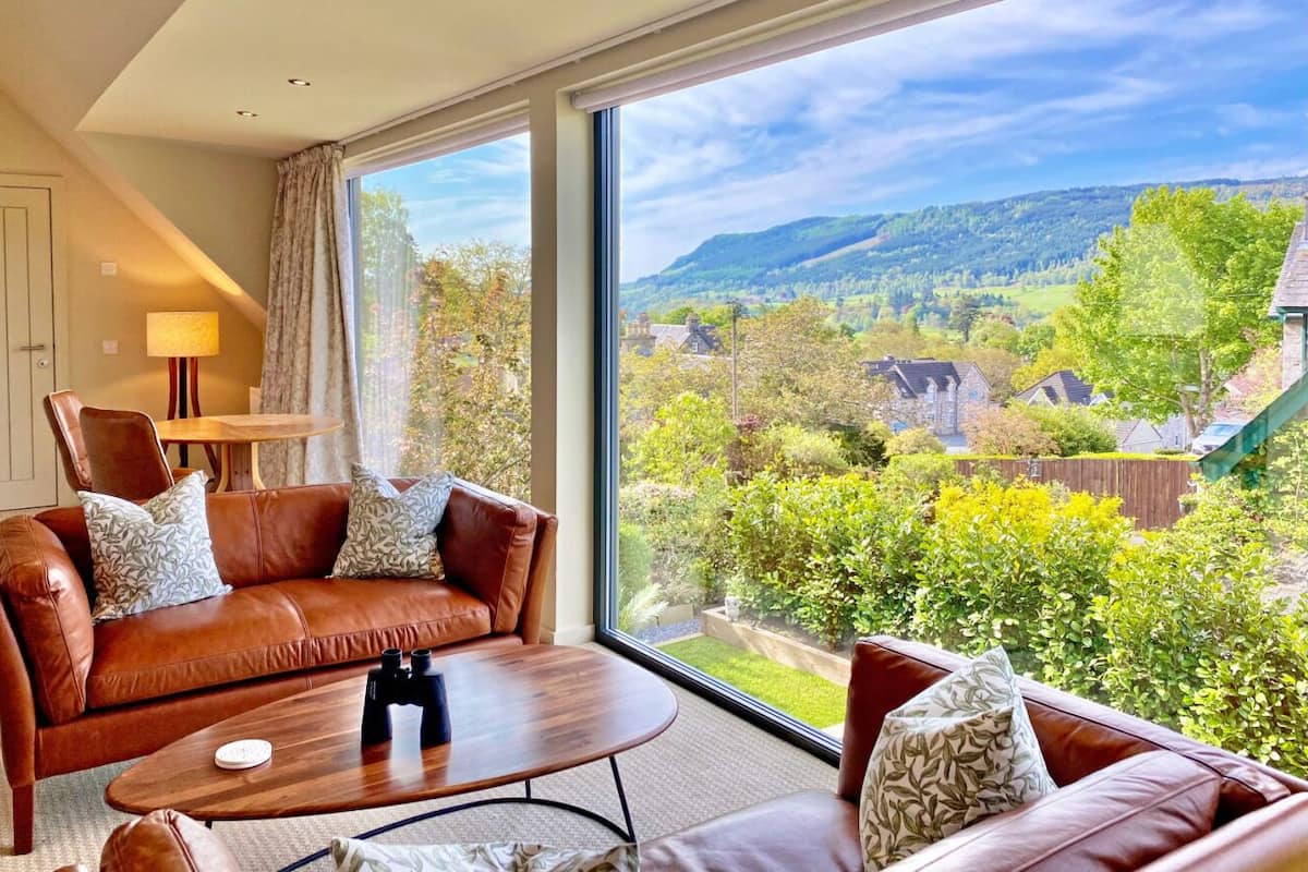 A modern hotel room with a large window offering a scenic view of hills and greenery.