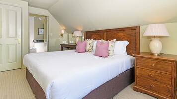 A neatly made bed with white linens and multiple pillows, a wooden nightstand with a lamp, and a door leading to a bathroom.