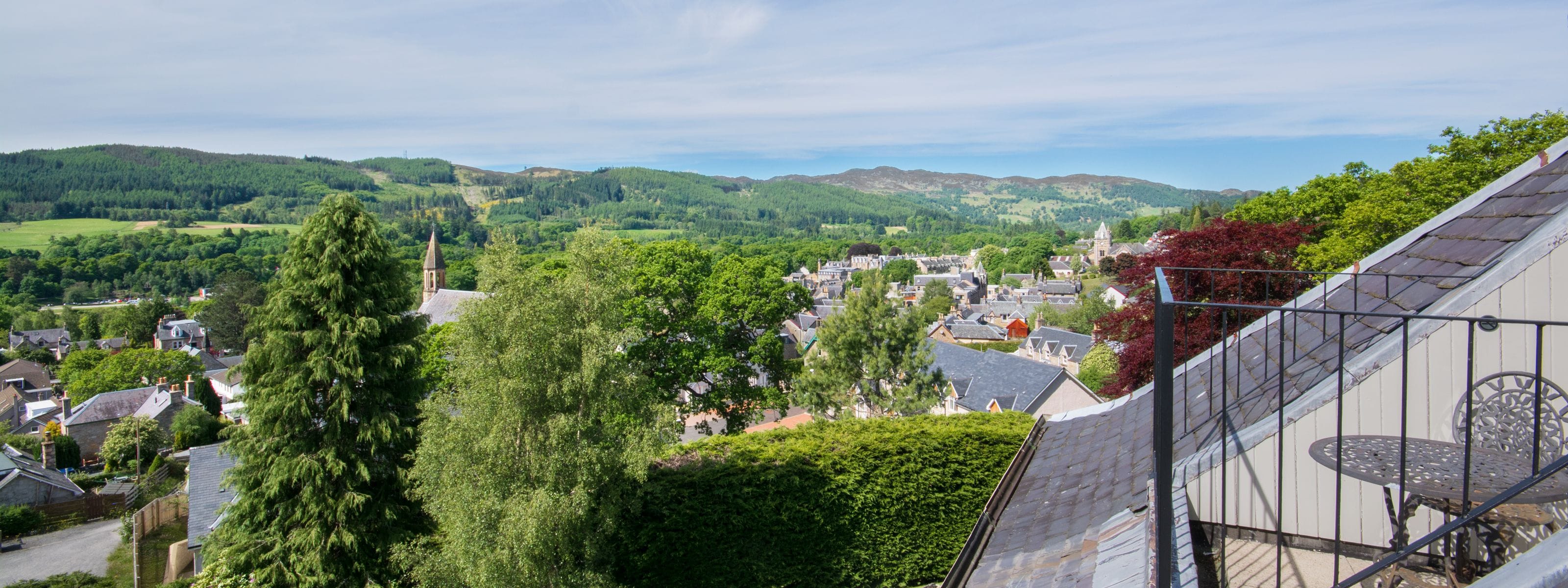 A town with a prominent church, lush green hills, and a view of a residential area with houses and trees.