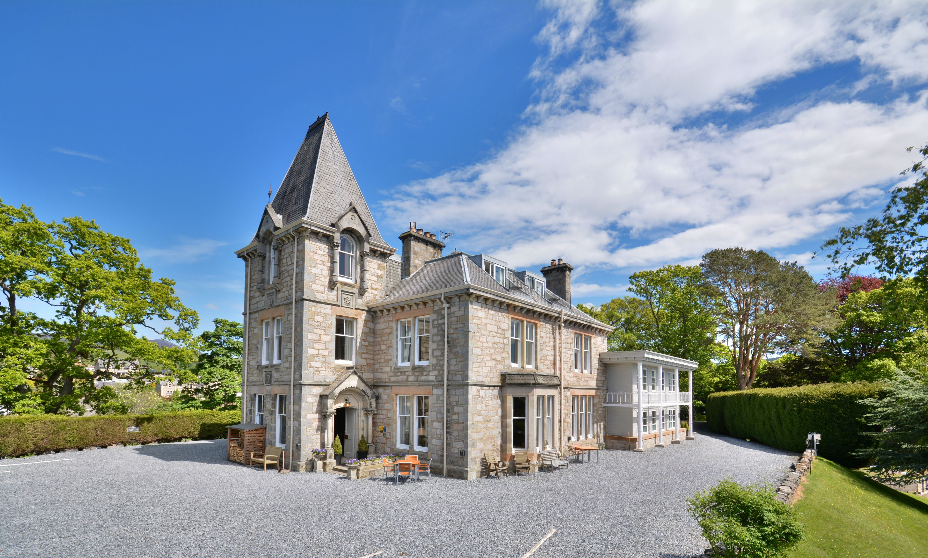 A large stone building with a prominent tower, multiple windows, and a gravel driveway.