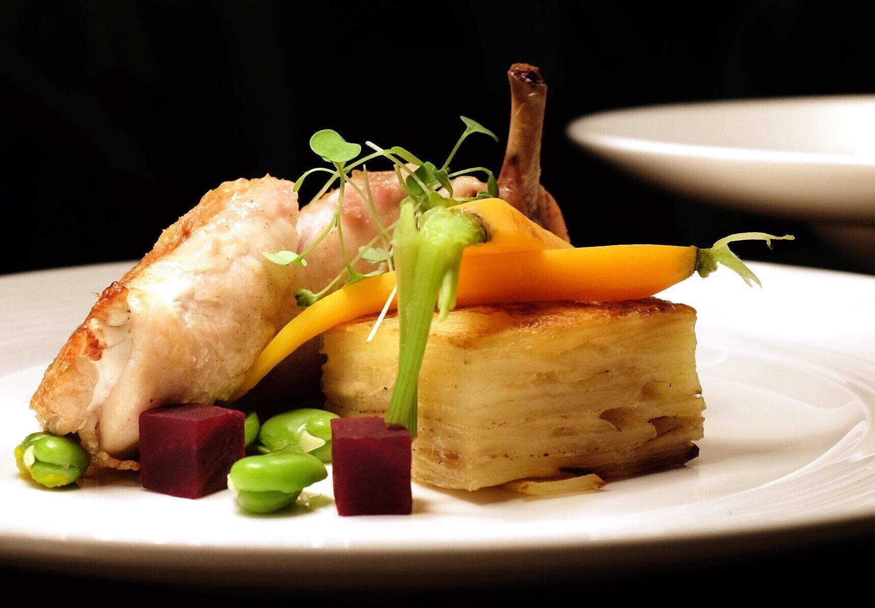 A plated dish with various food items including a piece of meat, vegetables, and a pastry.