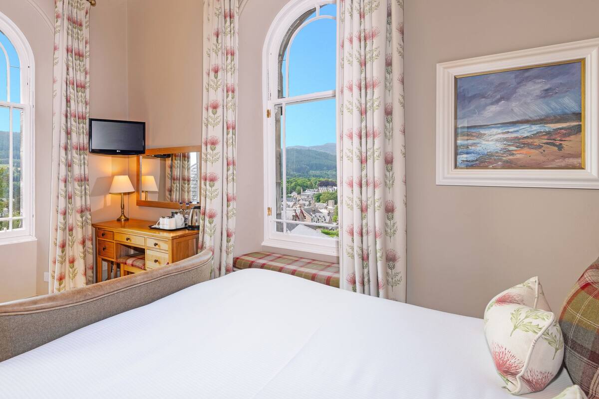 A hotel room with a large bed, a desk with a lamp, a television, and a painting on the wall.