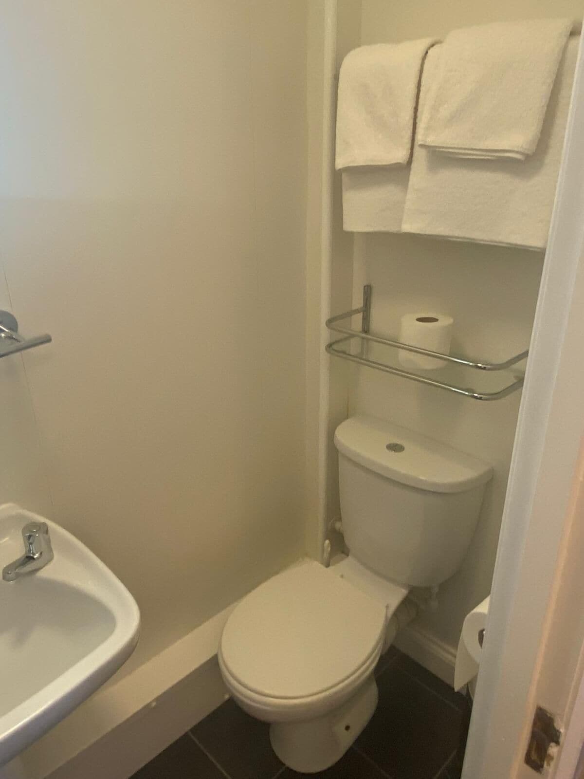 Ein kleines Badezimmer mit Toilette, Waschbecken und einer Glasablage mit Toilettenpapier.