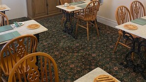 Een eetgedeelte met houten stoelen en tafels, een kroonluchter en een klok aan de muur.