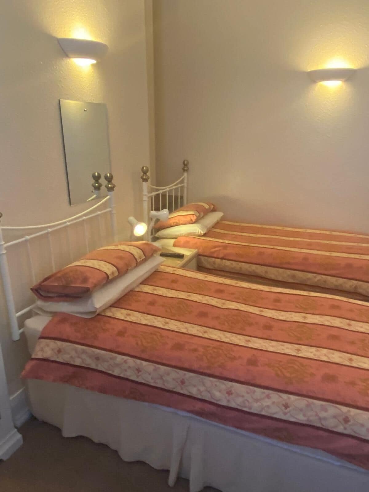 Una habitación con dos camas individuales, cada una con cabecera y lámparas de noche.